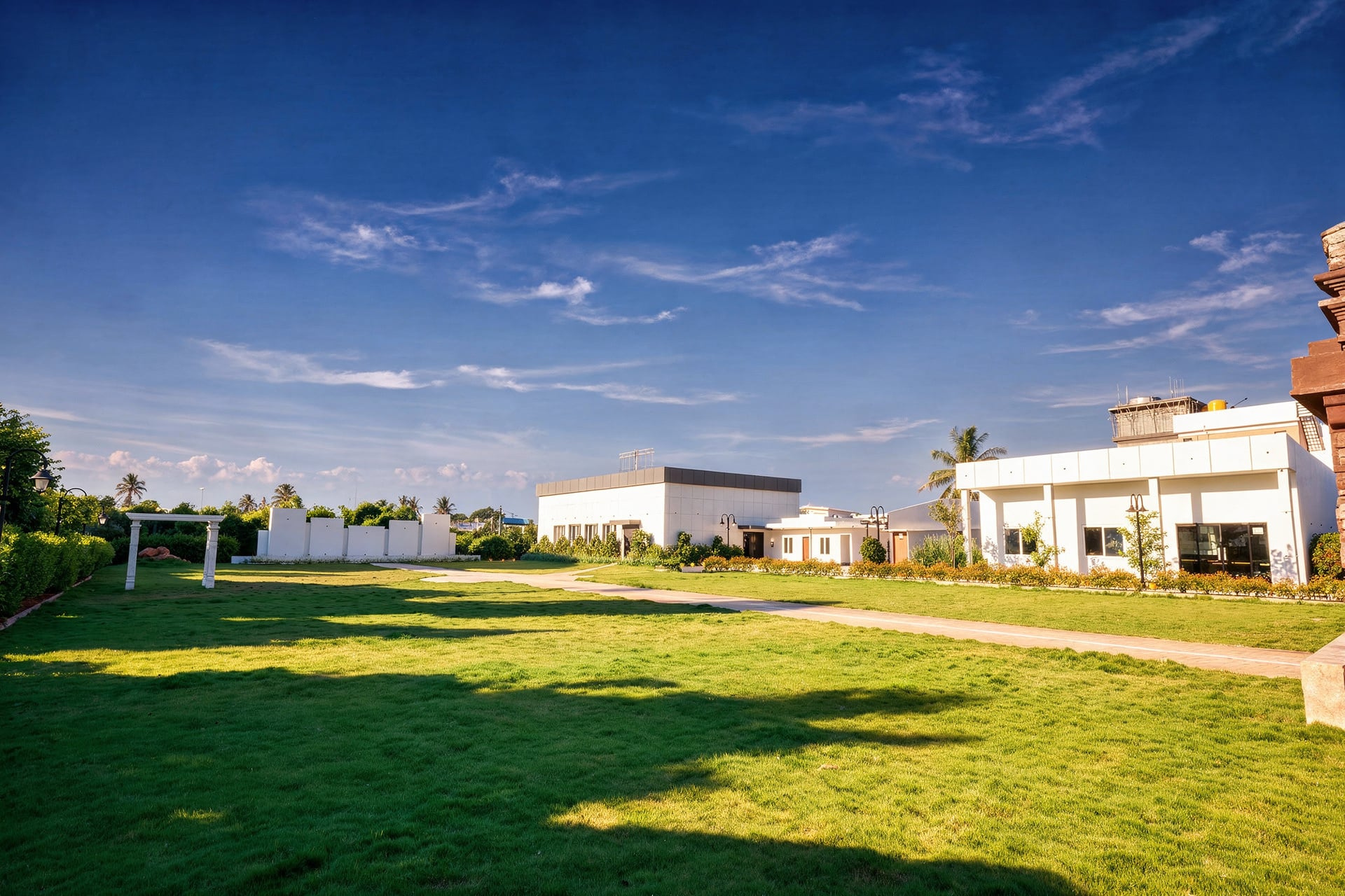 The open lawn at Sree Raaga Resorts on a clear day, with low white buildings along its far edge and a path across the grass