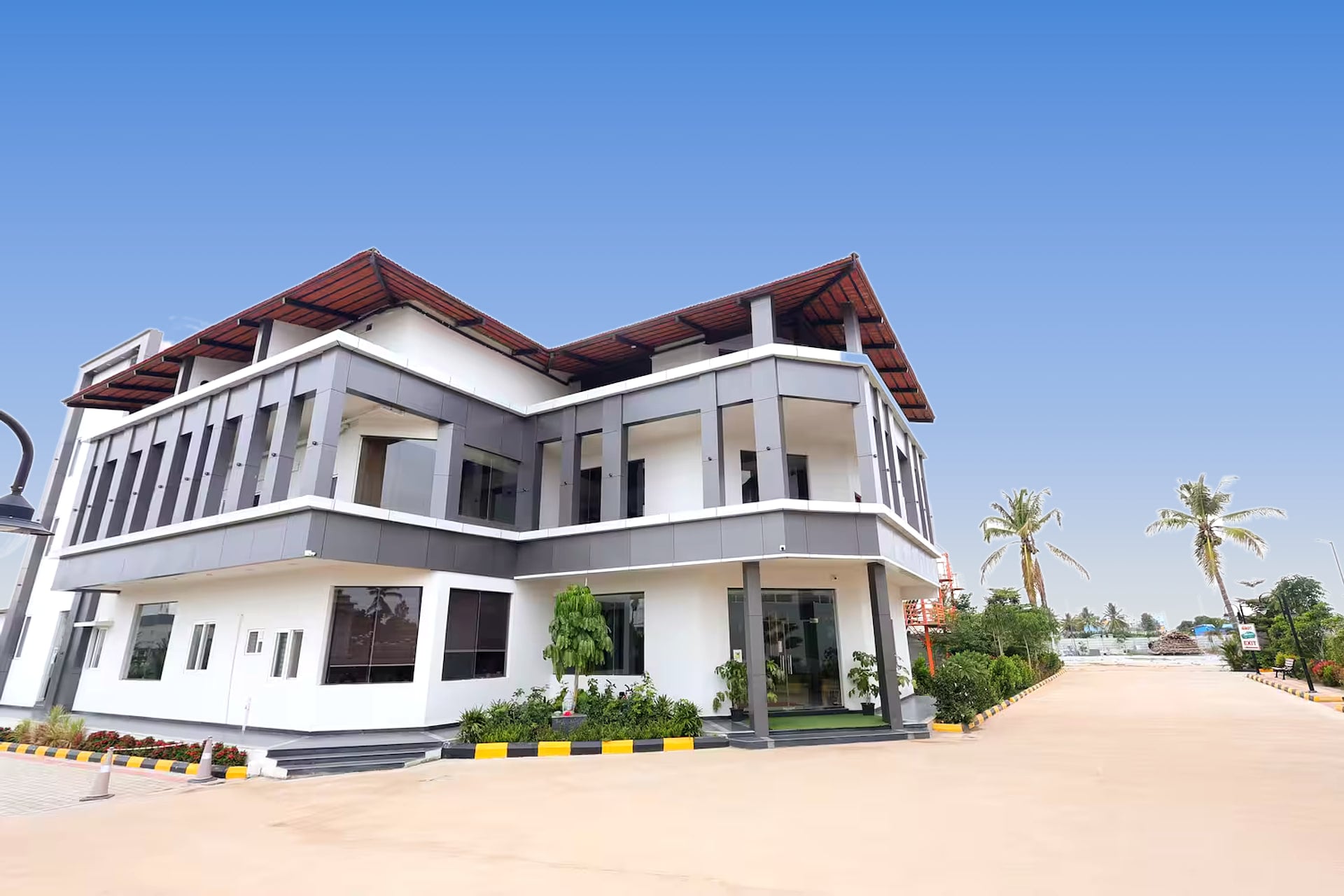 A three-storey white building at Sree Raaga Resorts with grey-framed balconies and a red pitched roof, beside a palm-lined drive