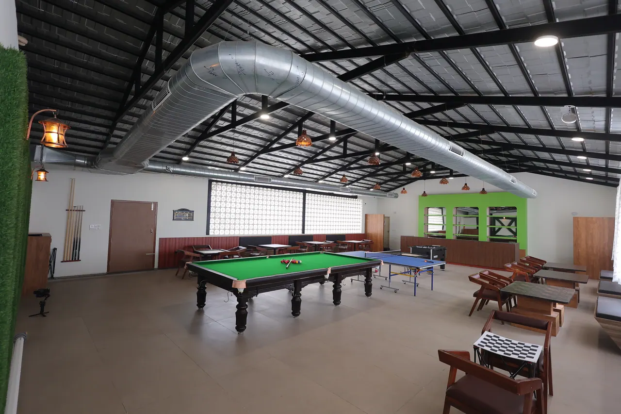 Indoor games hall under exposed steel trusses with a full-size snooker table, table tennis and foosball