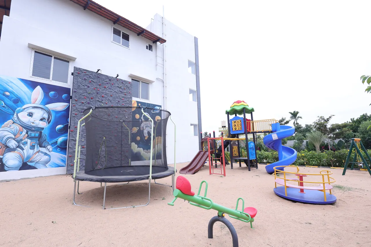 Children's play area with a netted trampoline, climbing wall, spiral slide, swings and roundabout