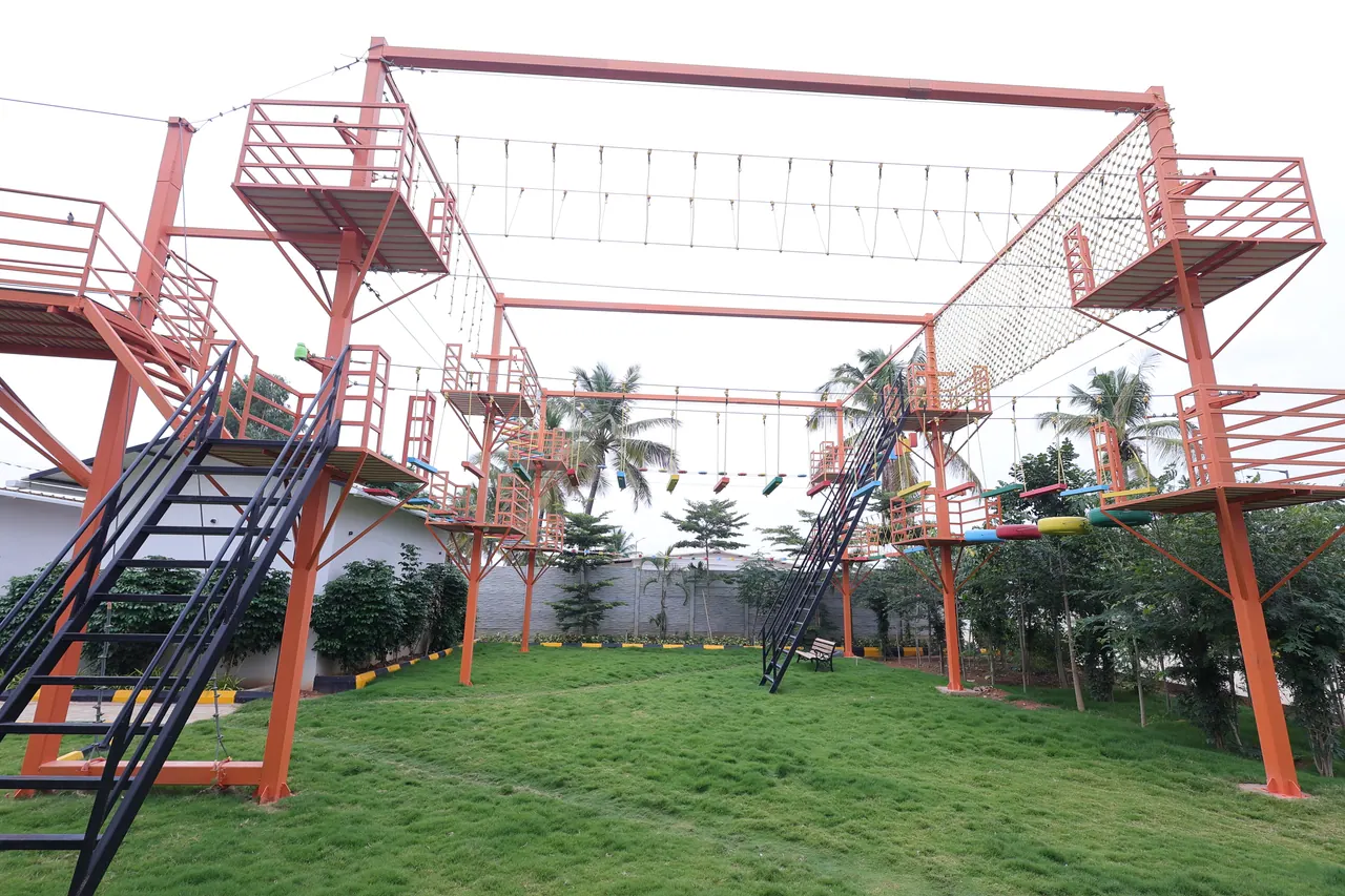 A large orange steel high rope course on a lawn with cargo nets, tyre steps and wire traverses