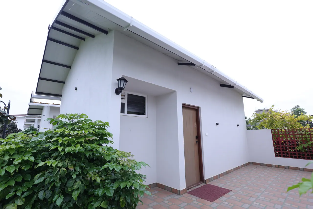 The private brick-paved forecourt and timber front door of a luxury villa, under a deep eave with a lantern