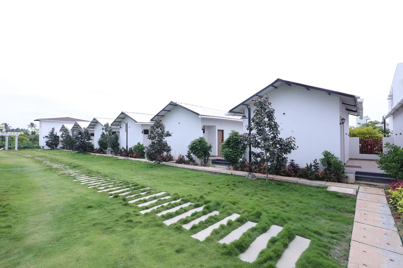 A row of single-storey white villas with pitched roofs, set along a mown lawn with a stepping-stone path
