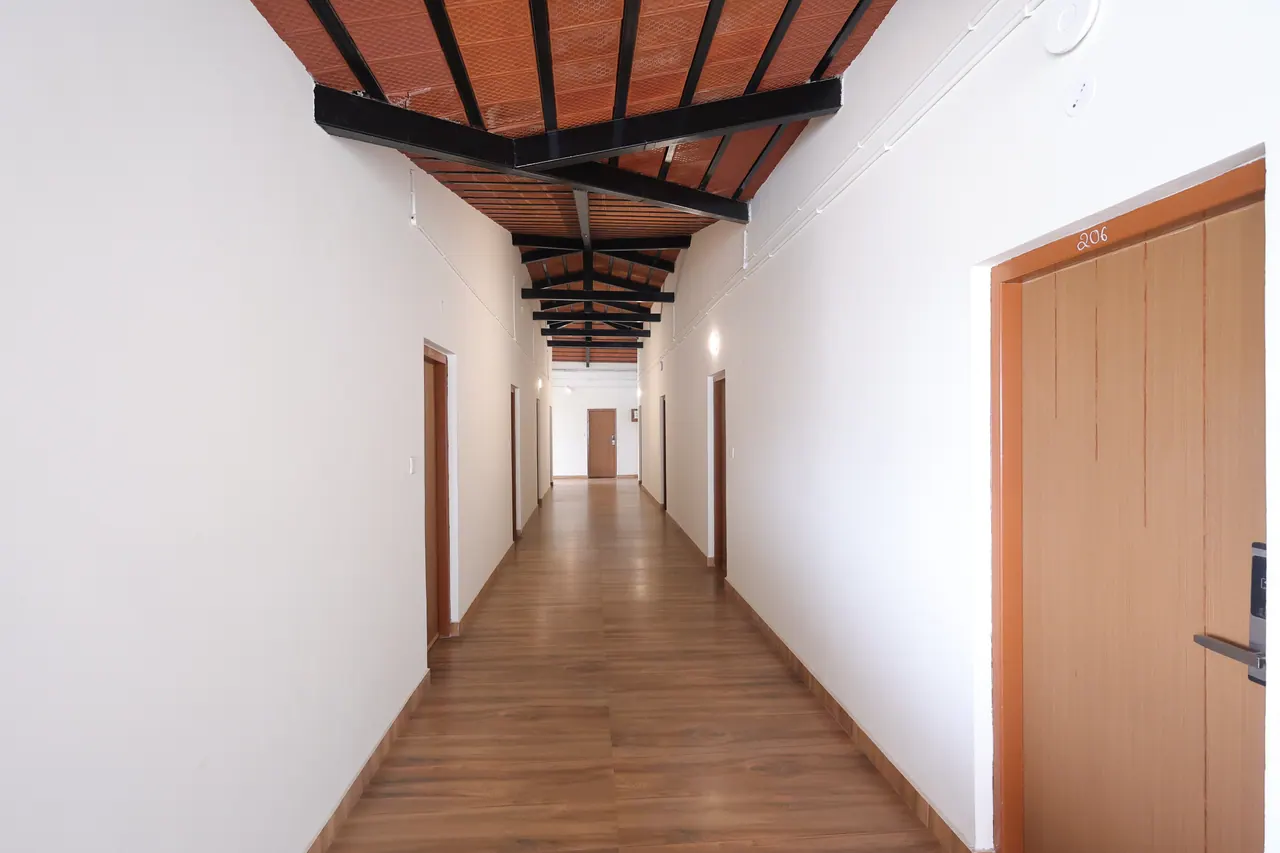 Guest corridor under an exposed pitched roof of black steel trusses and terracotta tile, with numbered timber doors