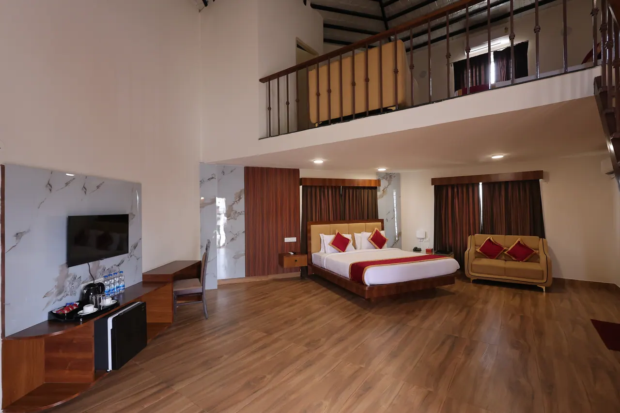 Double-height duplex living space open to an exposed steel-truss roof, with a king bed, sofa and mezzanine above