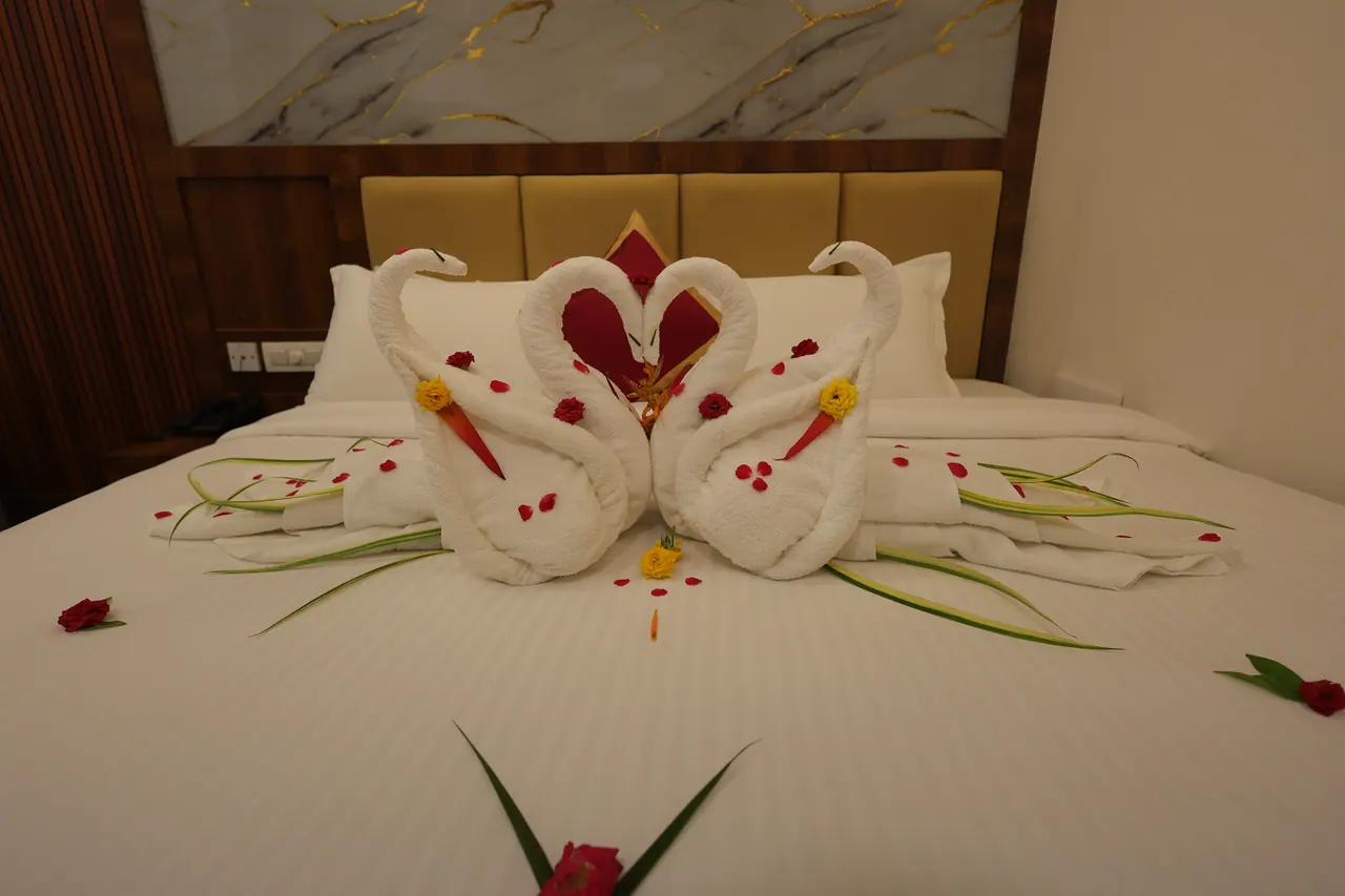 Two towels folded into swans with a heart, arranged on a villa bed